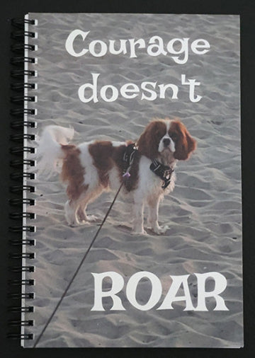 Journal with a dog on a leash on the beach, with text 'Courage doesn't roar'.