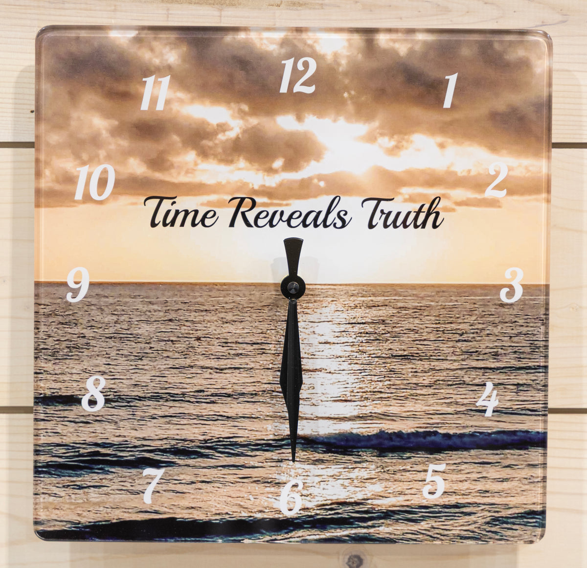 Square wall clock featuring a beach sunset. White Arabic numeral hour markers are placed over the scene, and the center reads the phrase 'Time Reveals Truth' in black script.