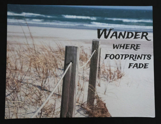 Canvas print with scenic beach scene with wooden fence and sand with 'Wander Where Footprints Fade' text.